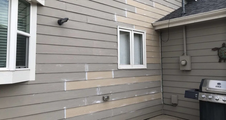 House corner in lap siding with new boards patched in among the old, not yet painted