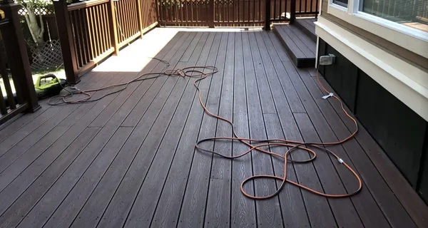 Dark brown composite deck with a railing and stairs down to the yard, an extension cord still lying on the boards