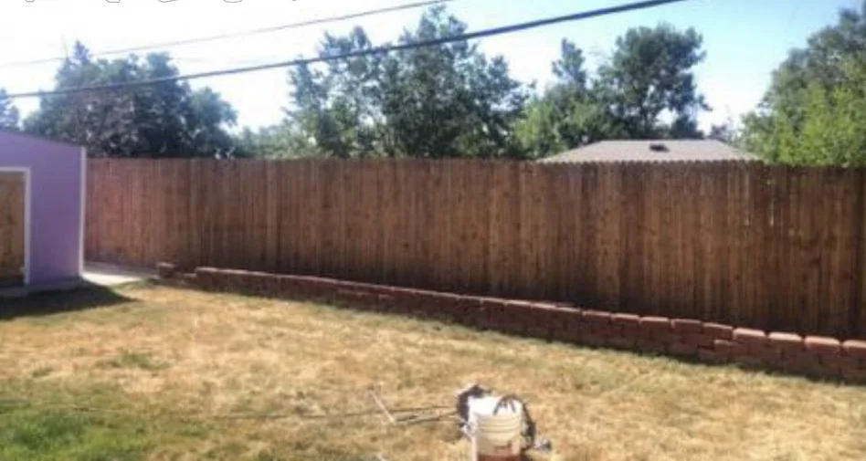 Long cedar privacy fence along a lawn, with a row of concrete edging blocks at its foot